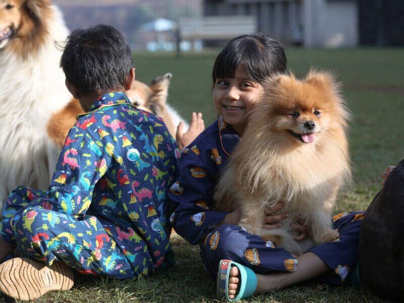Kids sitting on grass holding a smiling pomeranian
